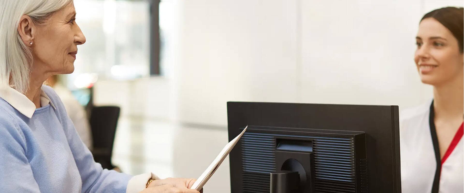 Elderly woman holding papers, speaking to a smiling Porsche Service Advisor